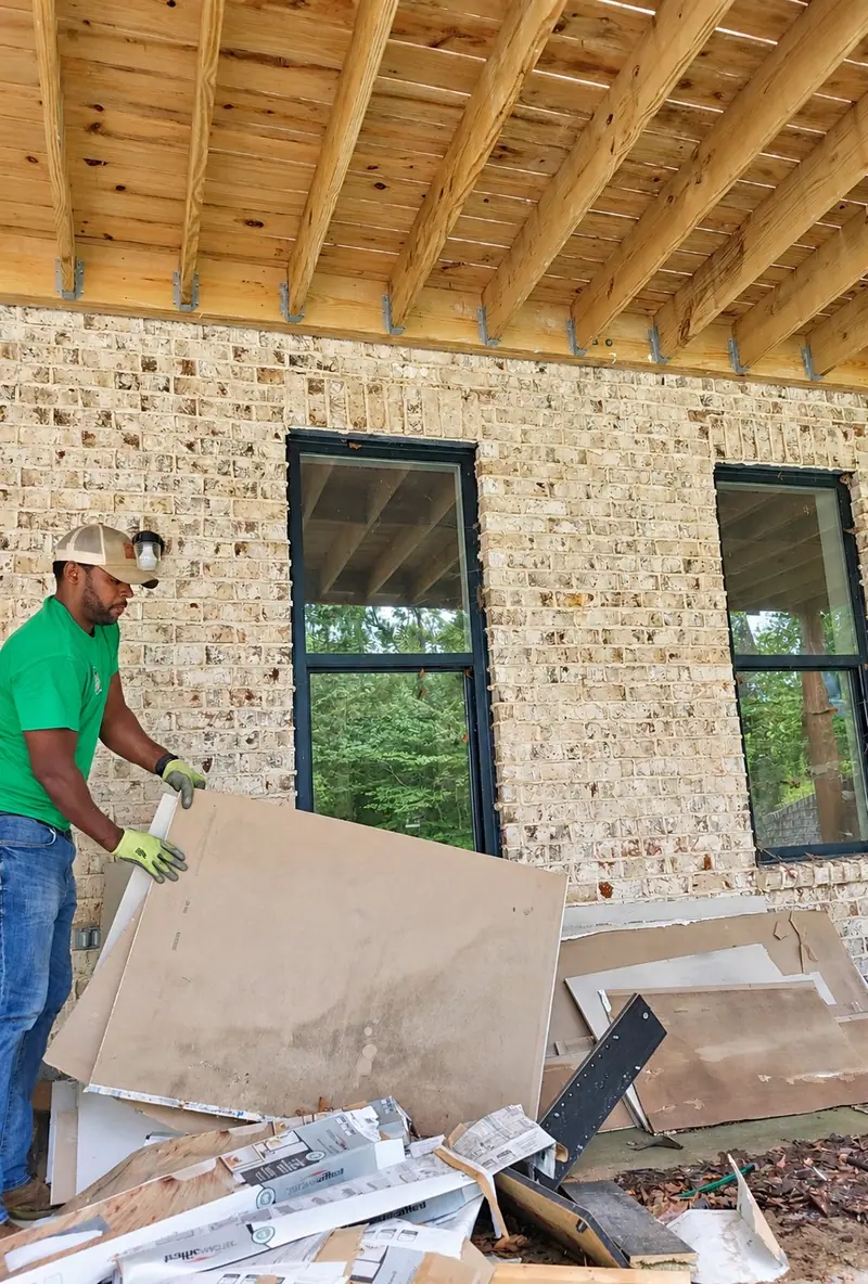 A crew member in a green Racoons shirt hauling drywall scraps off a new brick build