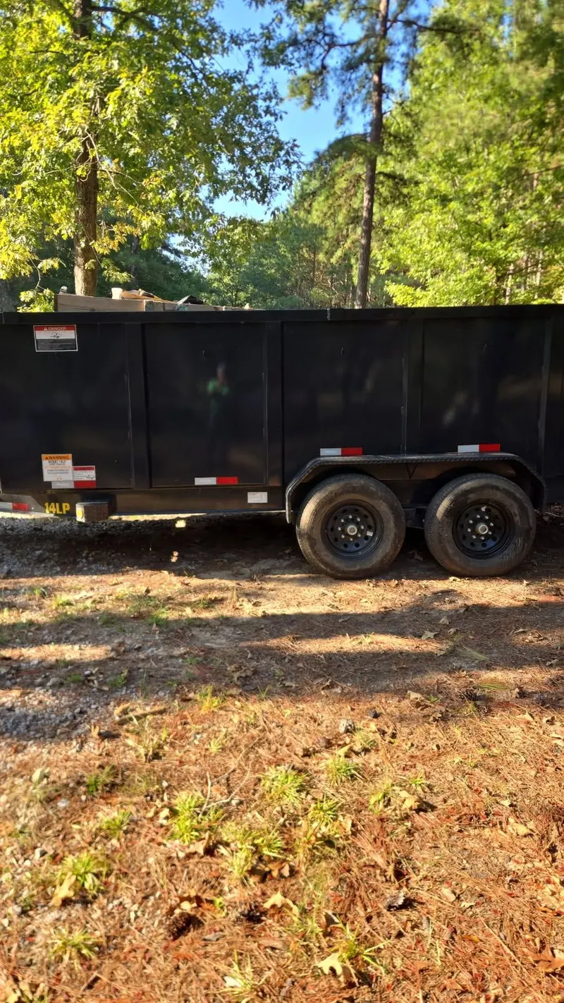 The Racoons dump trailer parked on a wooded job site, loaded with debris