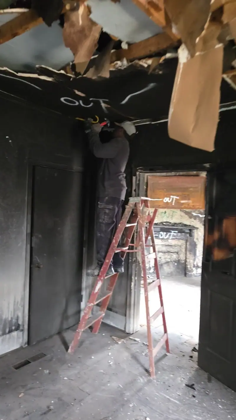 A Racoons crew member tearing out a fire-damaged ceiling