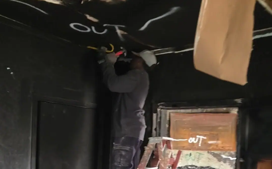 A Racoons crew member on a ladder pulling down a fire-damaged ceiling