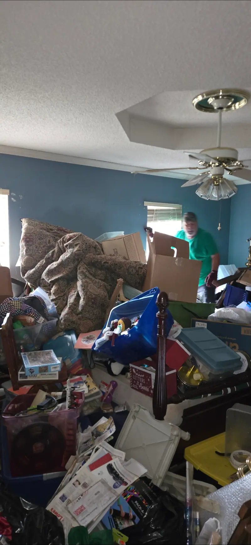 A crowded bedroom mid-cleanout, with a Racoons crew member in green working through it
