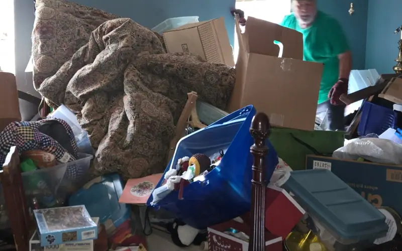 A crowded bedroom mid-cleanout, with a Racoons crew member in green working through it