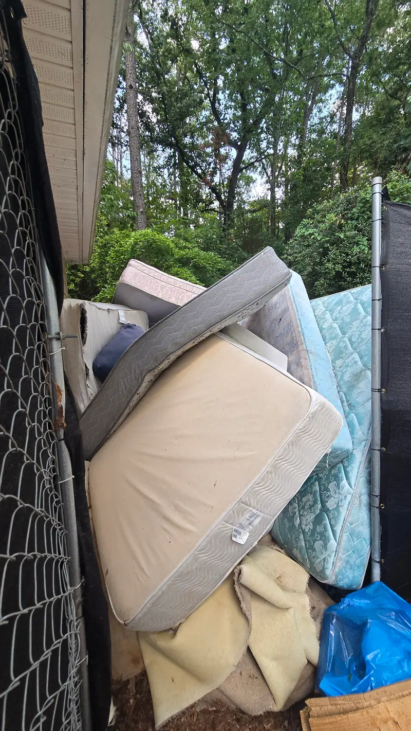 Old mattresses and box springs stacked by a fence for pickup