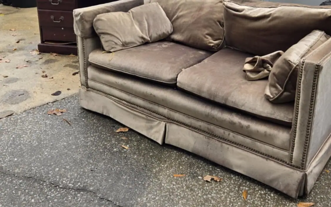 An old sofa and a wooden desk set out on a driveway for removal