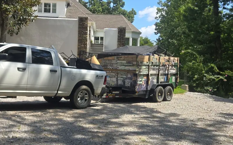 The white Racoons pickup towing the branded dump trailer, loaded and tarped, in a gravel driveway
